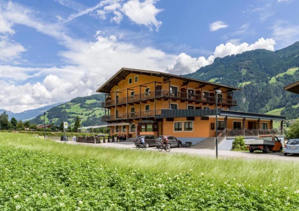 a large yellow building with mountains in the background at Sidan Hotel Restaurant & Pizzeria in Schwendau