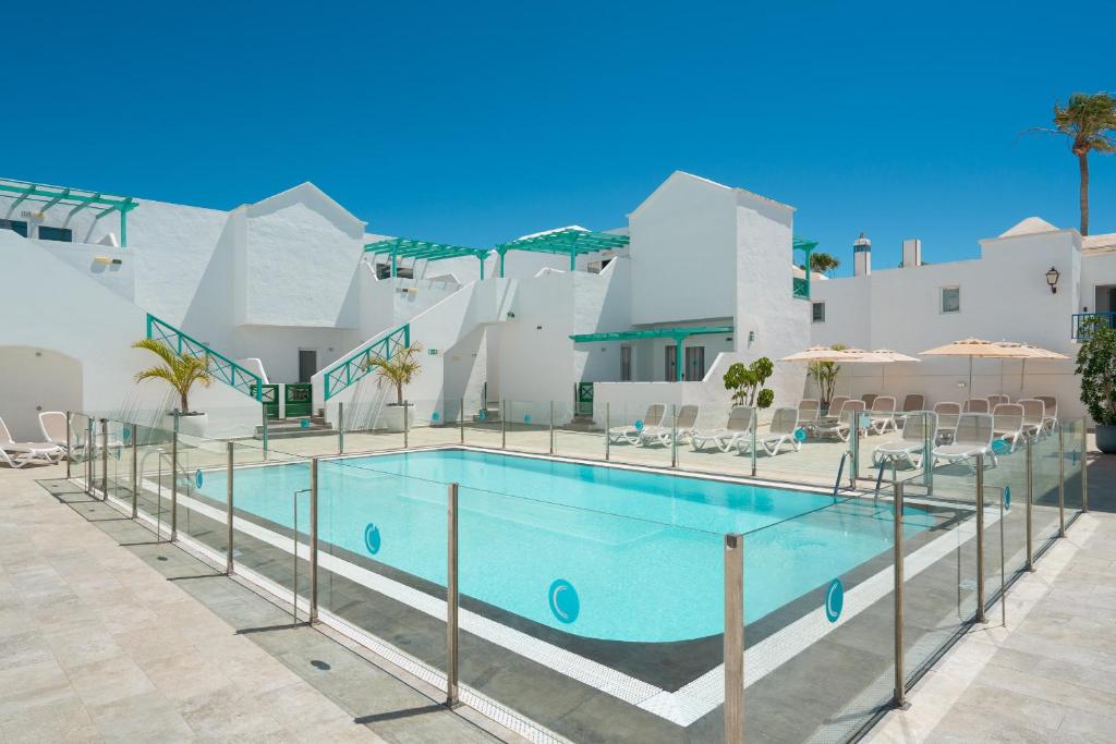 a pool with chairs and umbrellas in front of a building at Apartamentos Celeste in Costa Teguise