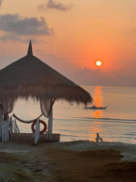 a beach with a straw umbrella and a boat in the ocean at JCAH BEACH HOUSE free WiFi in Araceli