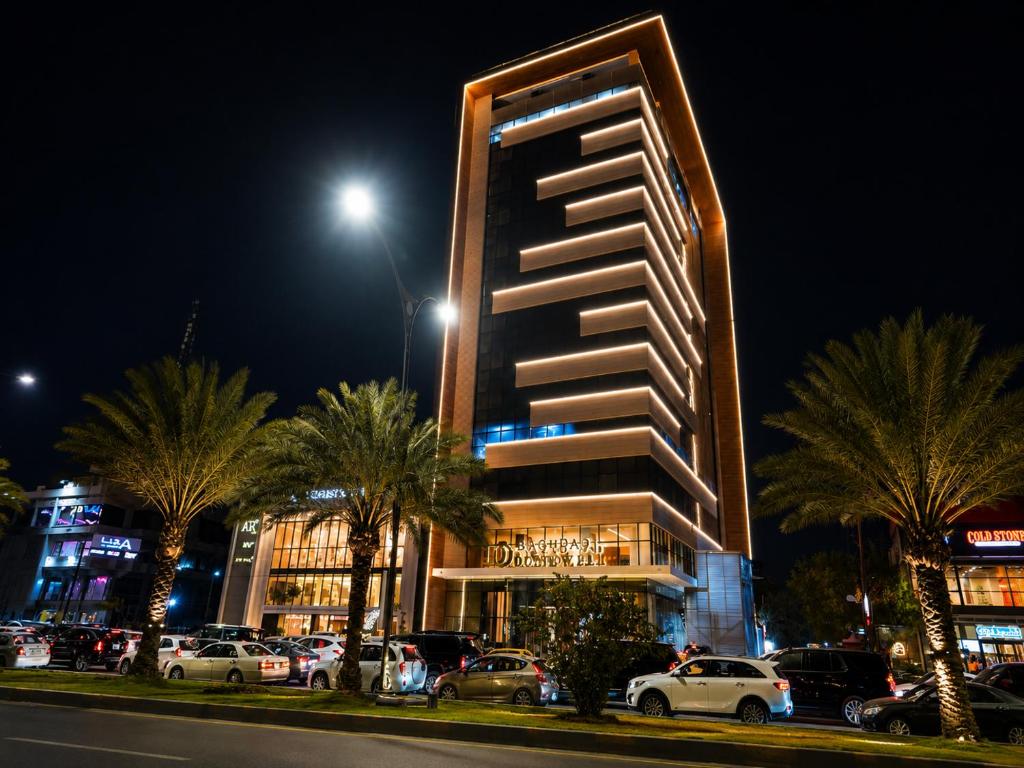 a tall building with cars parked in a parking lot at Baghdad Do Hotel in Baghdād