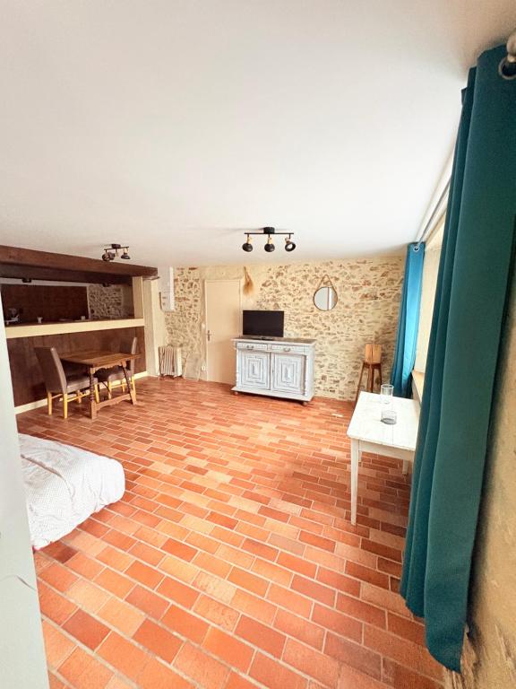 a room with a brick floor with a bed and a table at Charmant gite en pierre in Gratot