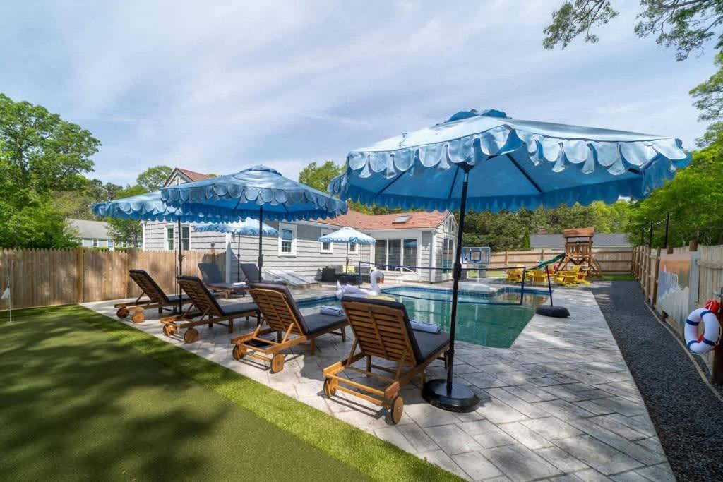 a group of chairs and umbrellas next to a pool at Cape Cod heated Pool, Putting Green, Speak Easy, Game room, in Harwich