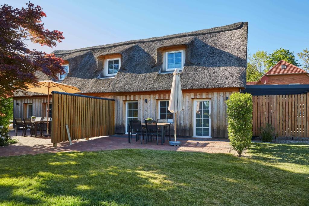 a house with a table and an umbrella in the yard at Reethaus M - Sommerhaus 54 in Grödersby