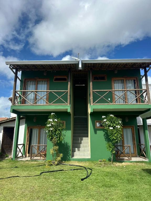 a green house with a balcony and grass at Pousada Tamikuã in Caraíva