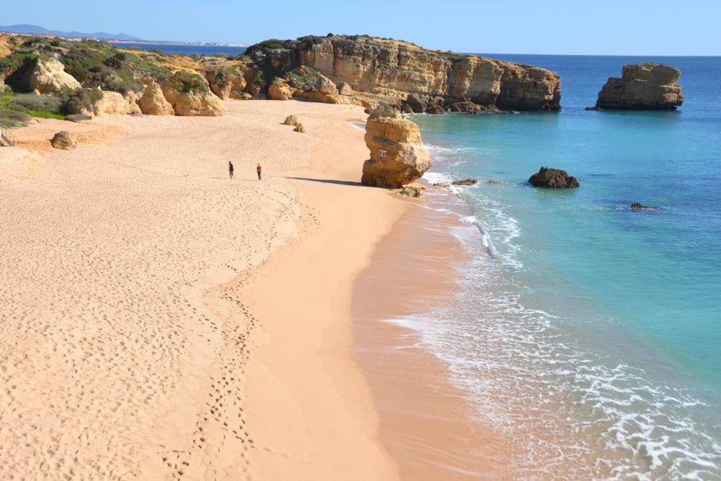people walking on a beach with rocks in the water at Apartment Sao Rafael in Albufeira