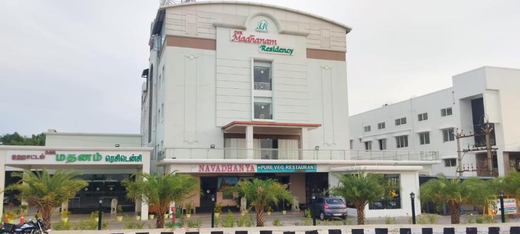 a large white building with palm trees in front of it at DsrMadhanamInn in Kumbakonam