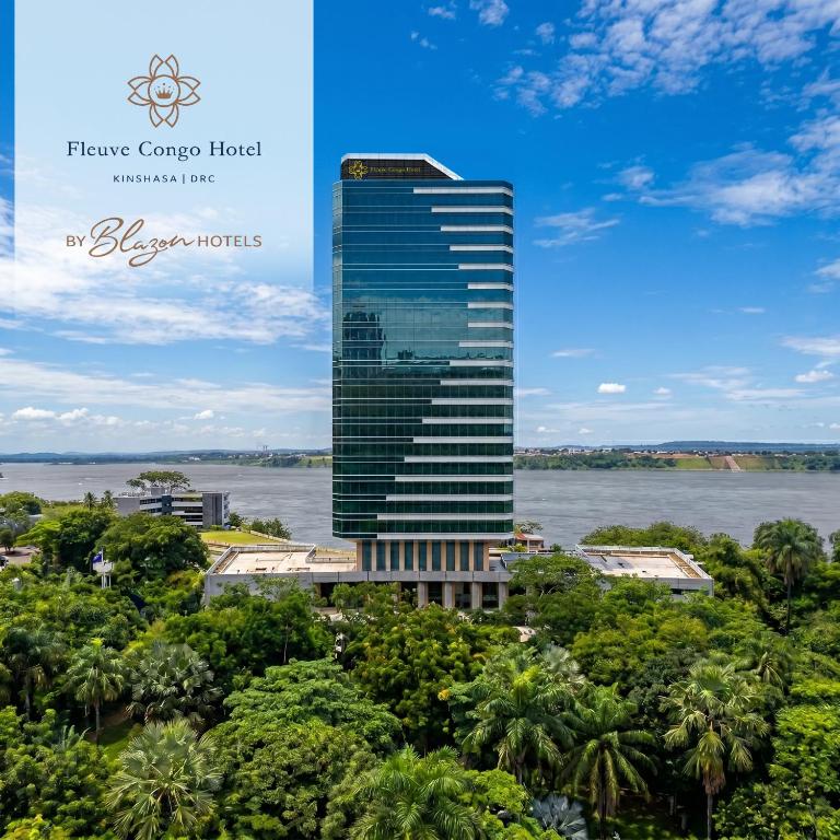 a tall building with trees in front of a river at Fleuve Congo Hotel By Blazon Hotels in Kinshasa