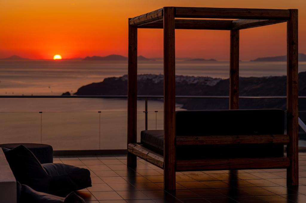 a chair sitting on a balcony with a sunset at Gizis Cliffside Suites in Imerovigli