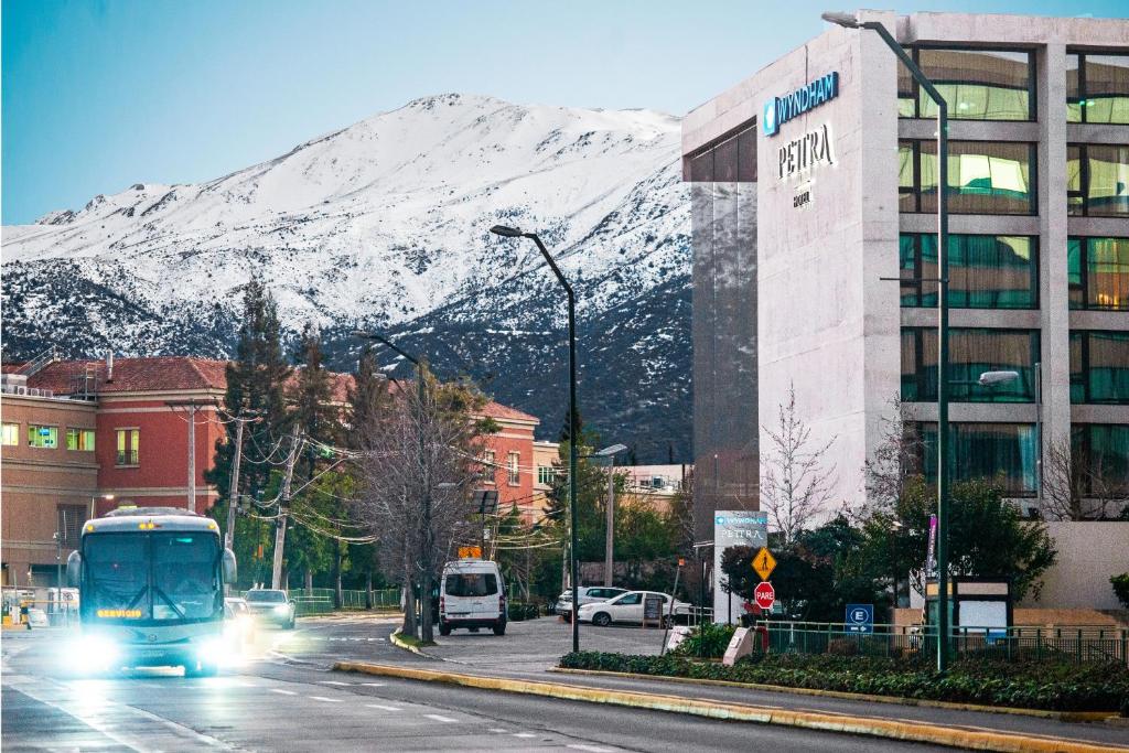 a bus driving down a city street with a snow covered mountain at Wyndham Santiago Pettra in Santiago