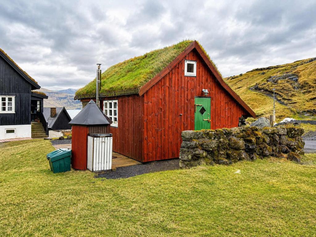 a red barn with a grass roof on a field at Traditional Cabin with Sea View in Stykkið