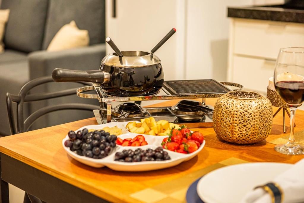 a plate of fruit on a table with a glass of wine at Apartamento com Café no 1º Dia, Kit Fondue e Aquecedor no Quarto a 300m da Praia para Casais in Imbituba