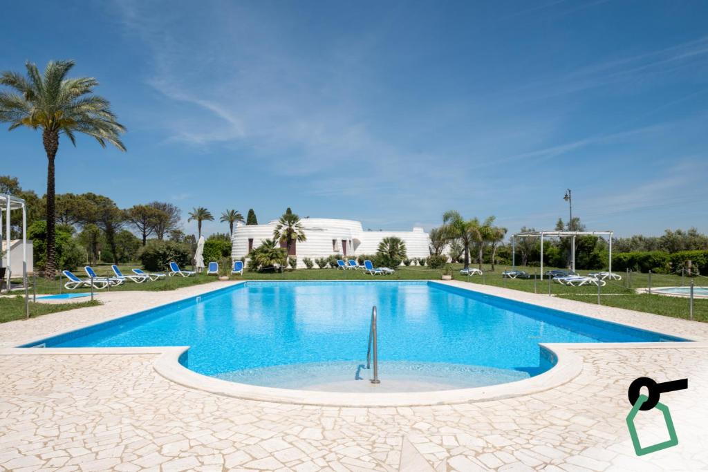 a swimming pool in a resort with palm trees and a building at Hotiday Gallipoli Masseria in Gallipoli