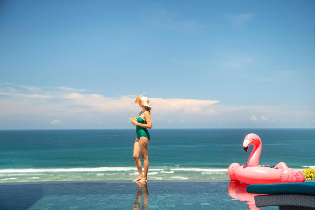 a woman standing on the beach next to a pink flamingo at Nusa Dua Cliff Ocean View with Private Beach in Nusa Dua