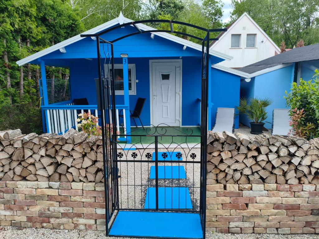 a blue house with a gate in front of it at Fenyőházak in Buzsák