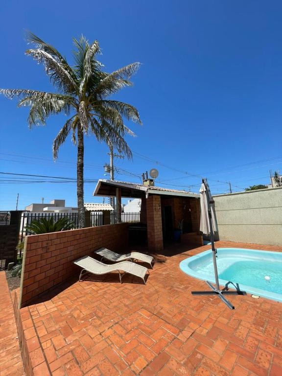 a swimming pool with two chairs and a palm tree at Ótima casa 3 quartos, piscina, bem localizada in Foz do Iguaçu