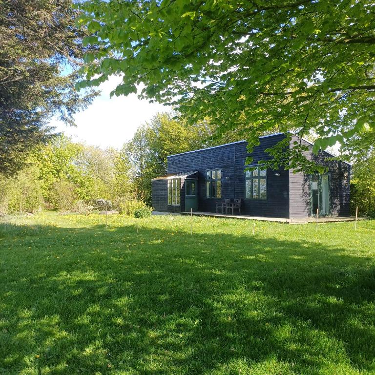 a black house in a field with a green yard at Agerdal - dejligt hus midt i mark og have in Nykøbing Mors