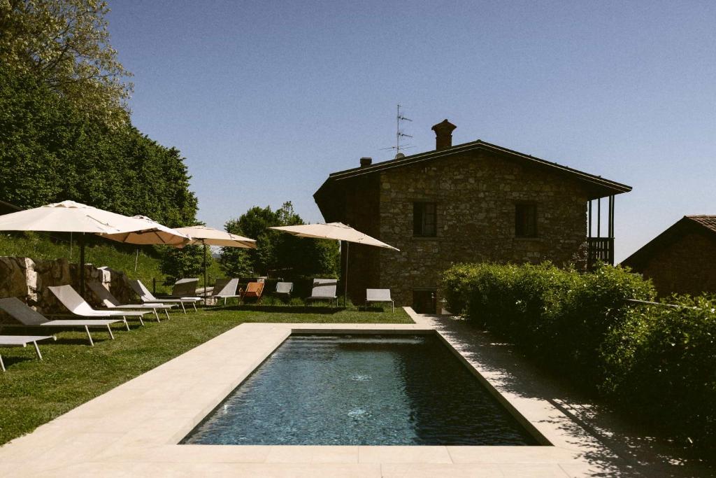 a swimming pool with chairs and umbrellas next to a building at Cascina Belvedì in Clanezzo