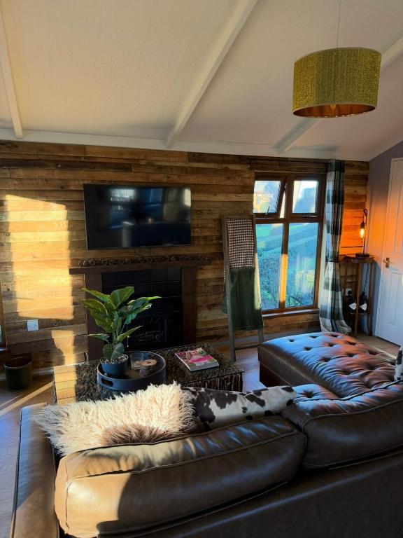 a living room with a leather couch and a fireplace at Woodside Lodge, Weybourne, Holt in Weybourne