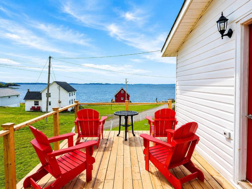 a deck with four red chairs and a table at Long Beach Lookout Vacation Rental in Twillingate