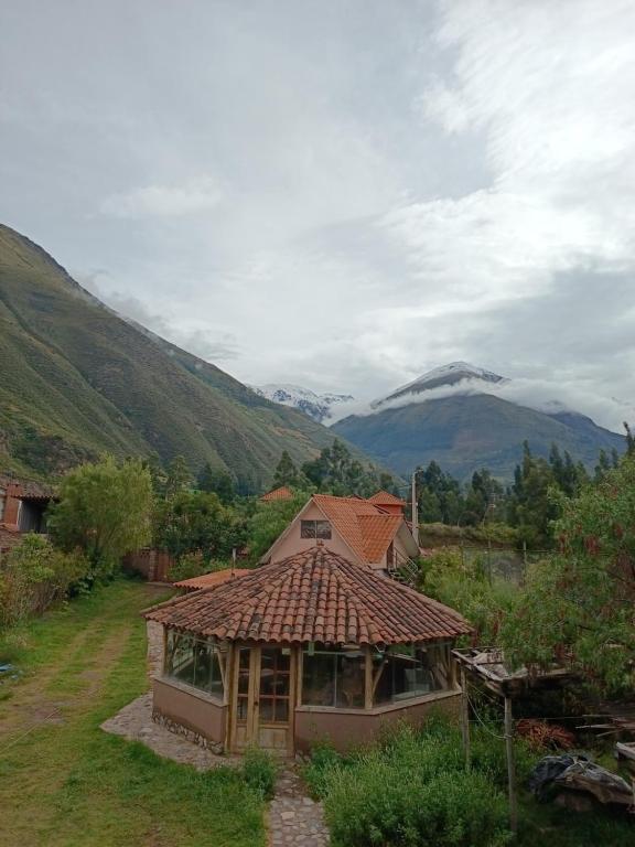 a house with a tiled roof with mountains in the background at Mrs Sapo Chalets in Urubamba