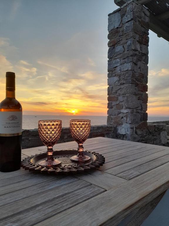 a bottle of wine and two wine glasses on a table at il mare stone house with Aegean view in Agios Dimitrios