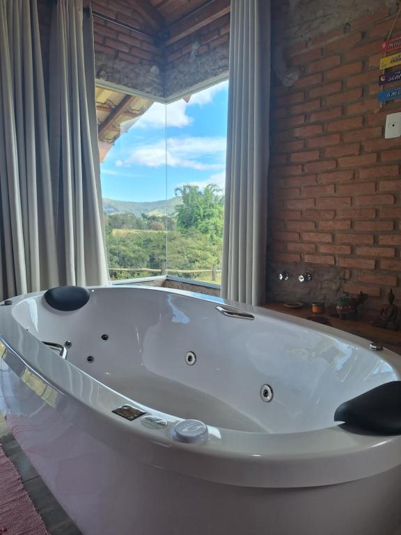 a bath tub in a room with a large window at Chalé Água Santa in São Thomé das Letras