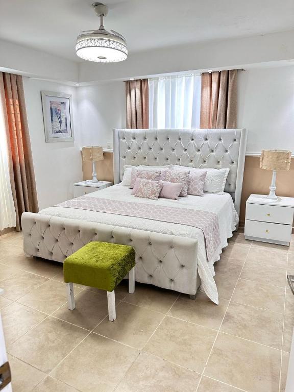 a white bedroom with a large bed and a green stool at Franco Residence in Santiago de los Caballeros