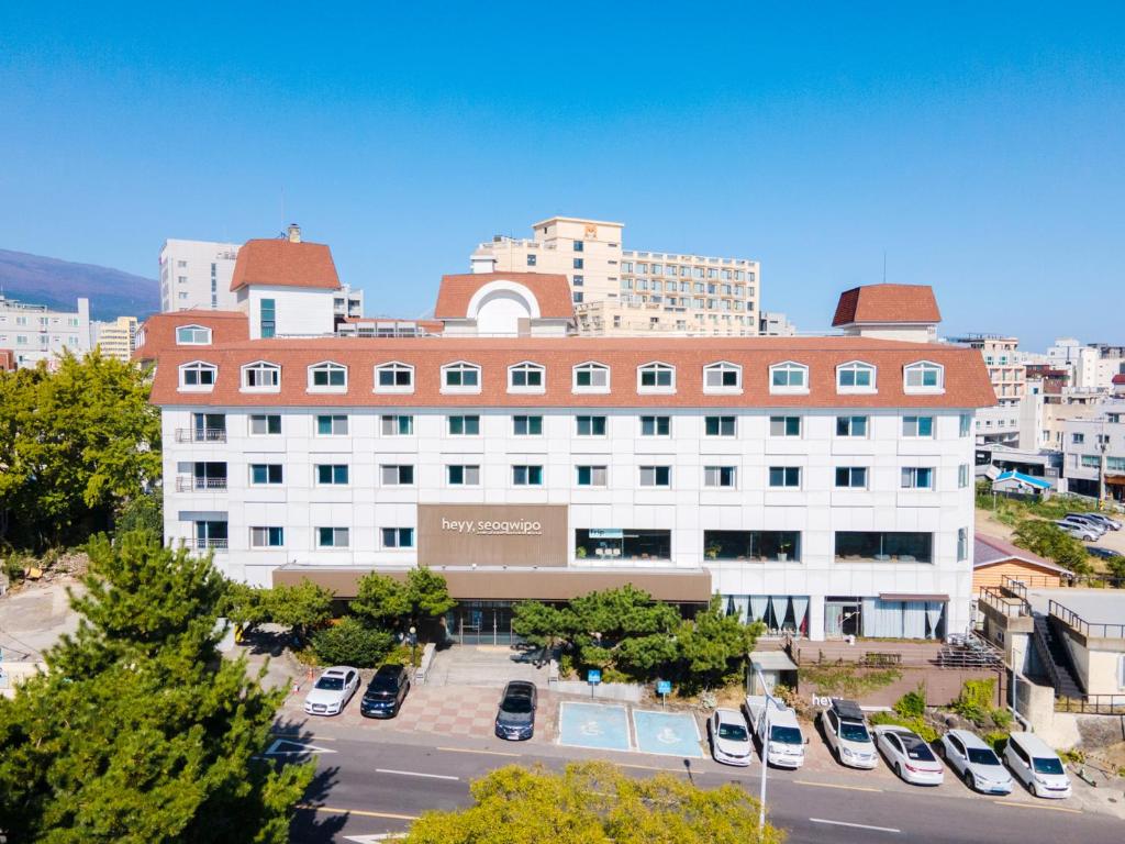 a large white building with cars parked in a parking lot at Heyy Seogwipo Hotel in Seogwipo