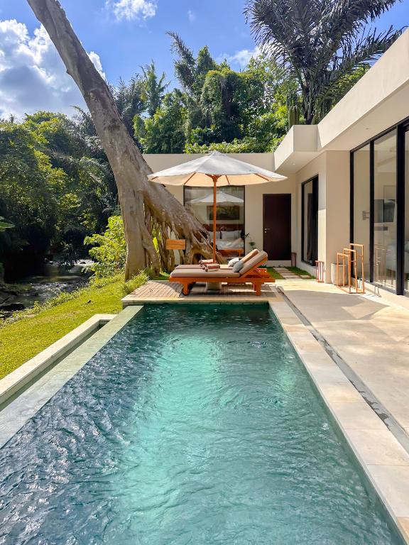 a swimming pool with chairs and an umbrella next to a house at 3BR Tala Villa Ubud in Ubud