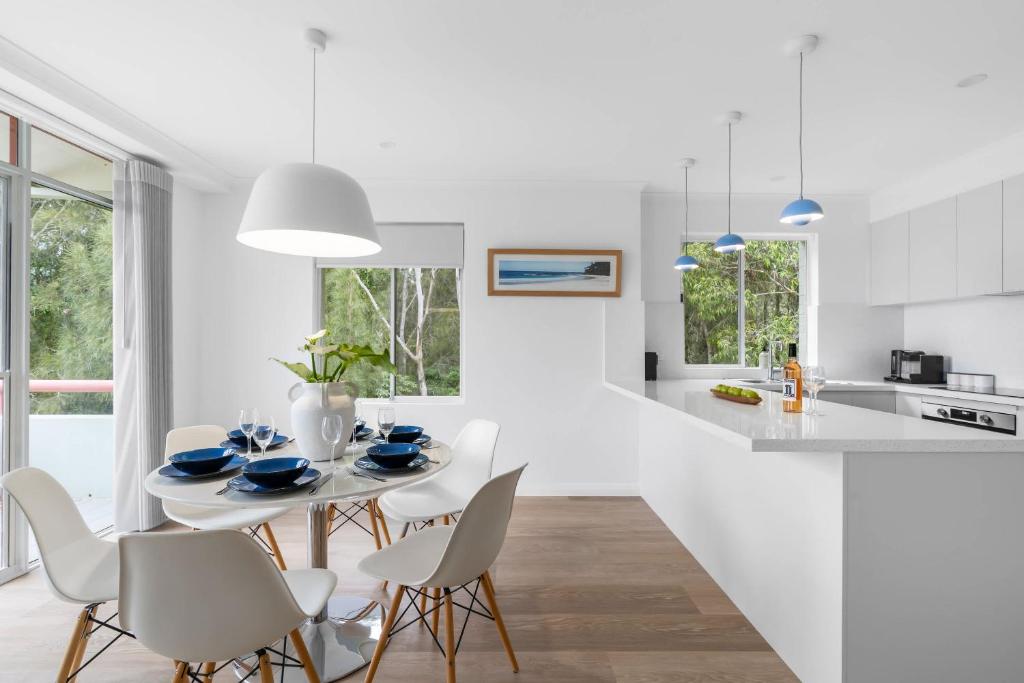 a white kitchen and dining room with a table and chairs at Fathoms 13 Mollymook Beach in Mollymook