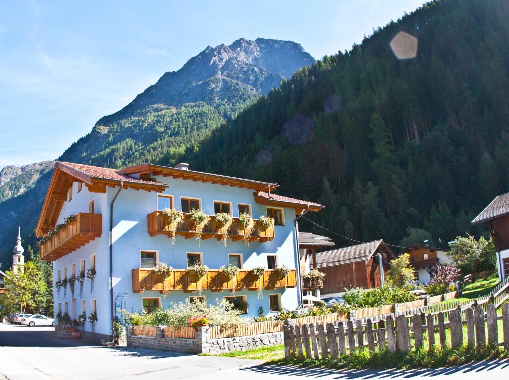 ein weißes Gebäude mit einem Zaun vor einem Berg in der Unterkunft Tirolerhof - Appartmenthaus in Kaunertal