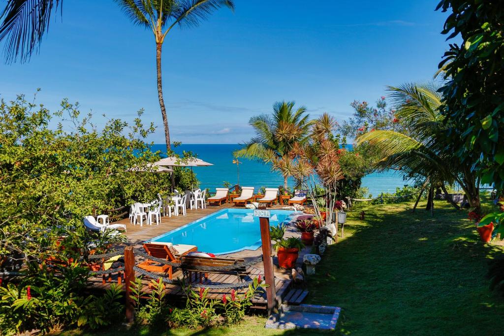 um resort com uma piscina e cadeiras e o oceano em Pousada Jakuara em Arraial d'Ajuda