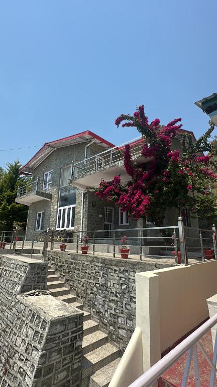 a building with a stone wall and a tree with pink flowers at Vrishti Homestay in Bhīm Tāl