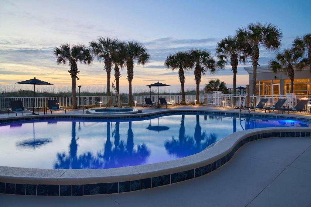 a swimming pool with palm trees and a building at Courtyard by Marriott Jacksonville Beach Oceanfront in Jacksonville Beach