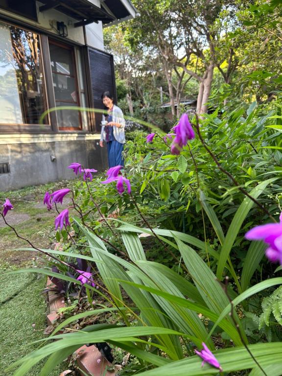 a man standing in a garden with purple flowers at ＯＫＵＮＯ ＩＥ in Oshima