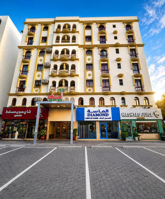 a large white building with shops in front of it at Alreef Hotel Suits in Muscat