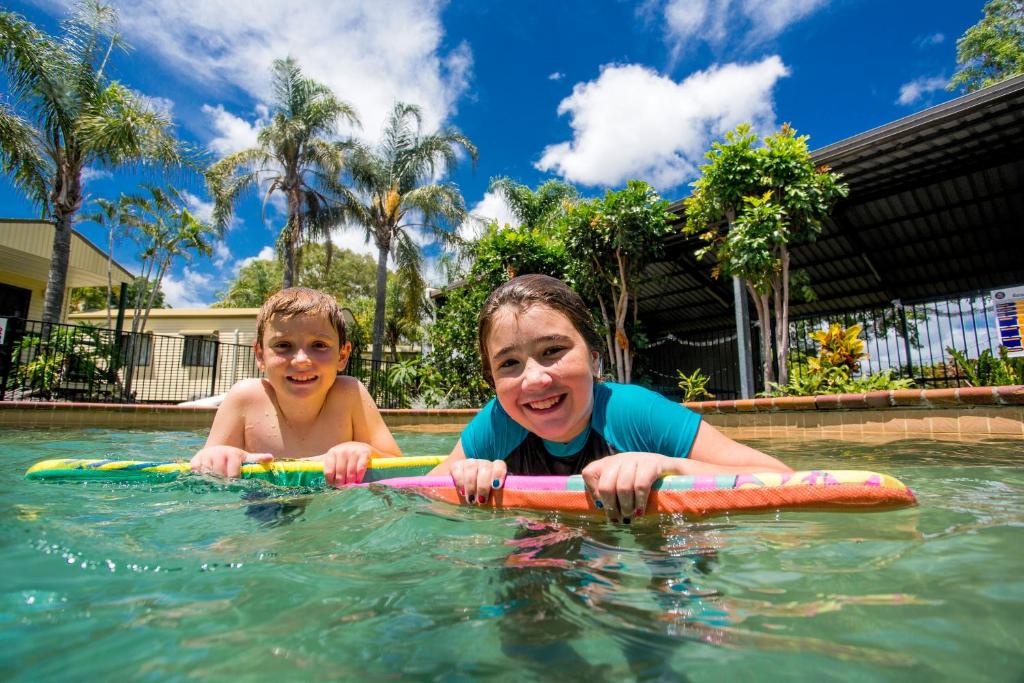 two girls are sitting in the water with a surfboard at Tasman Holiday Parks - Hervey Bay in Hervey Bay