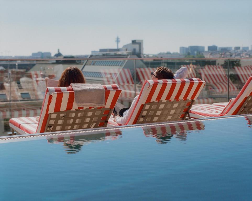 two people sitting in lawn chairs next to a swimming pool at Grand Ferdinand Vienna – Your Hotel In The City Center in Vienna