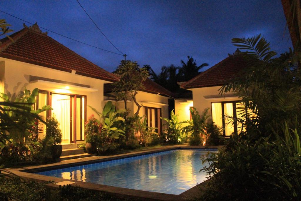 a swimming pool in front of a house at night at Uma Budhas in Ubud