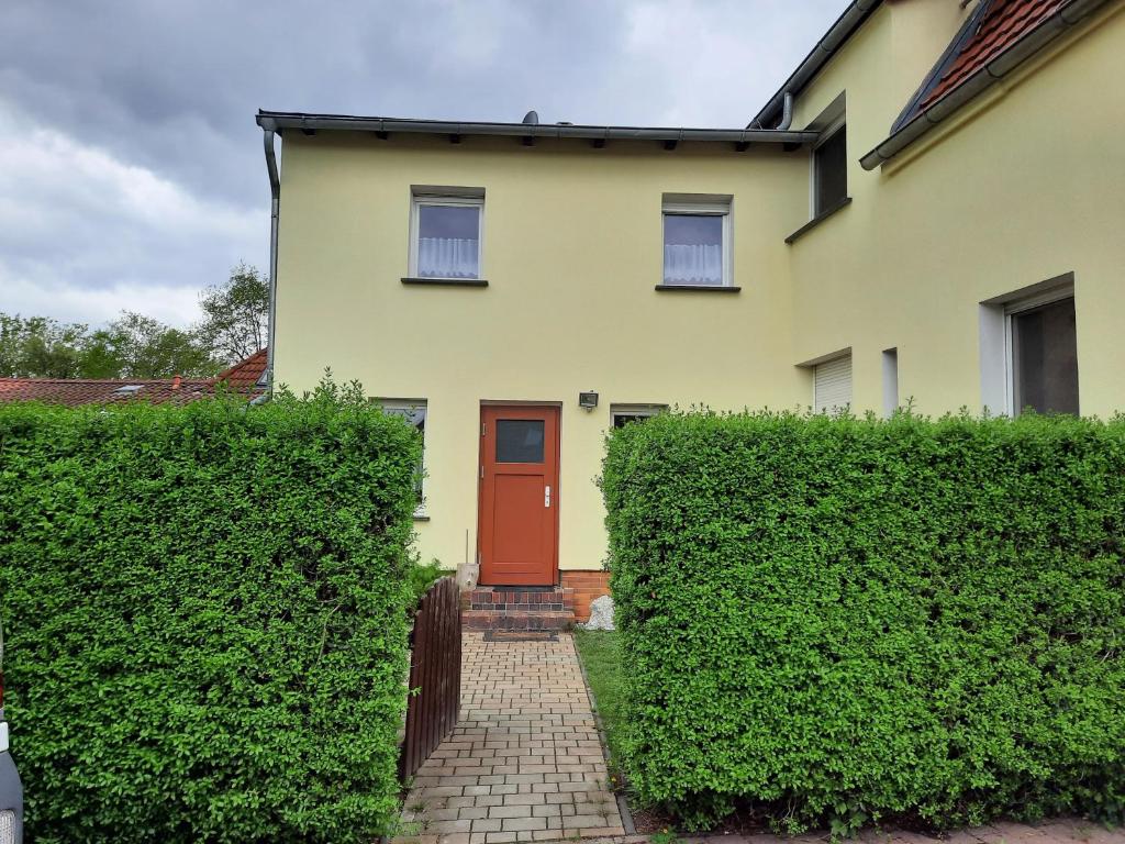 a yellow house with a red door and some bushes at Kastanienhof Lübben in Lübben