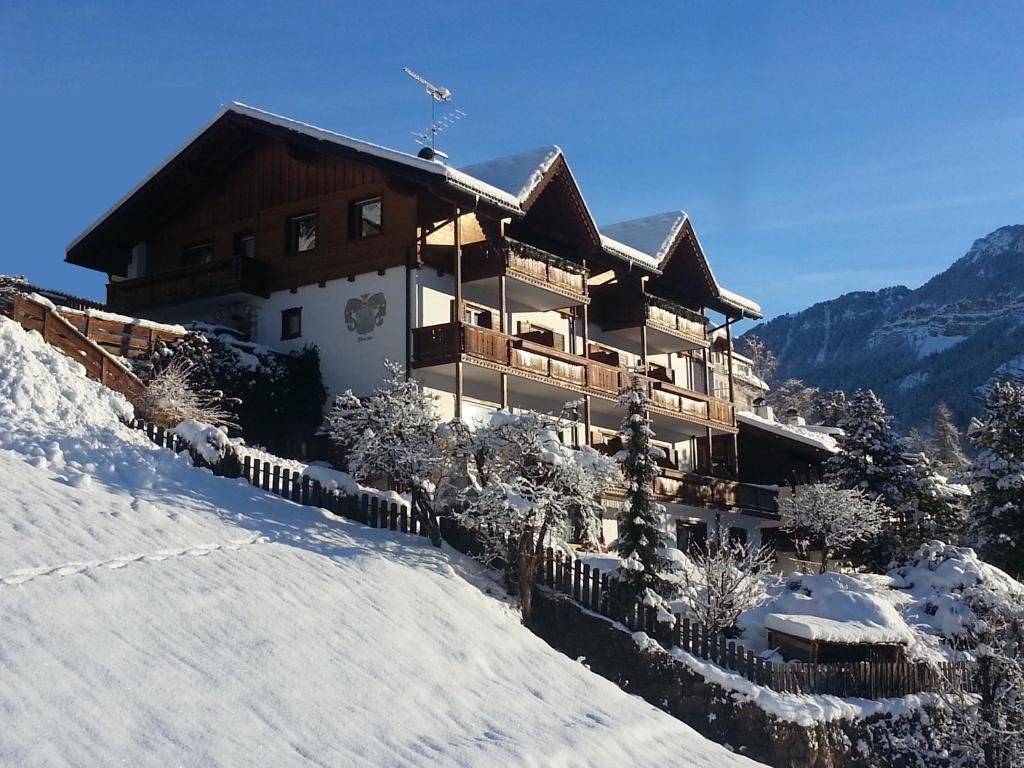 une maison avec un bâtiment située sur une colline enneigée dans l'établissement Garni Alba Bed & Breakfast, à Ortisei