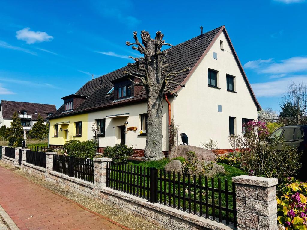 a white house with a tree in front of a fence at Ferienwohnung "Baum" in Rechlin