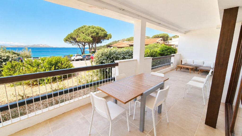 a balcony with a wooden table and chairs and the ocean at Rena Bianca Residence 201 in Baja Sardinia