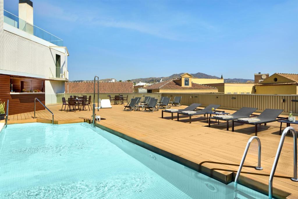 ein Swimmingpool auf dem Dach eines Gebäudes mit Holzterrasse in der Unterkunft NH Málaga in Málaga