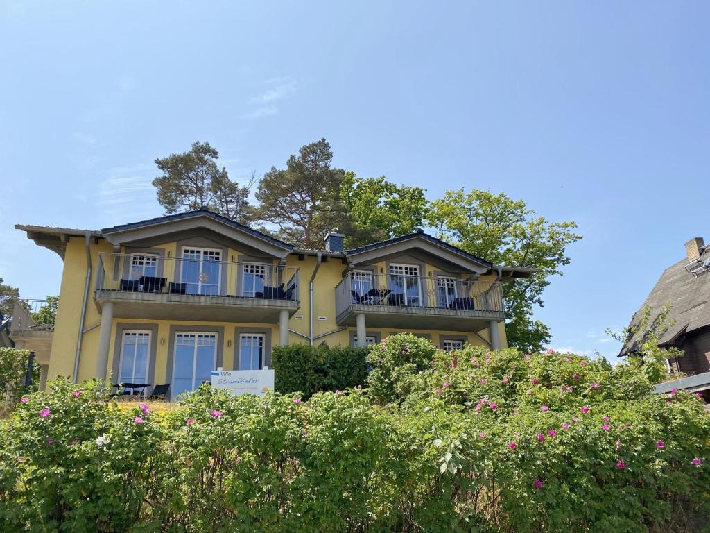 a yellow house with a balcony on top of some bushes at Haus Strandkiefer in Baabe