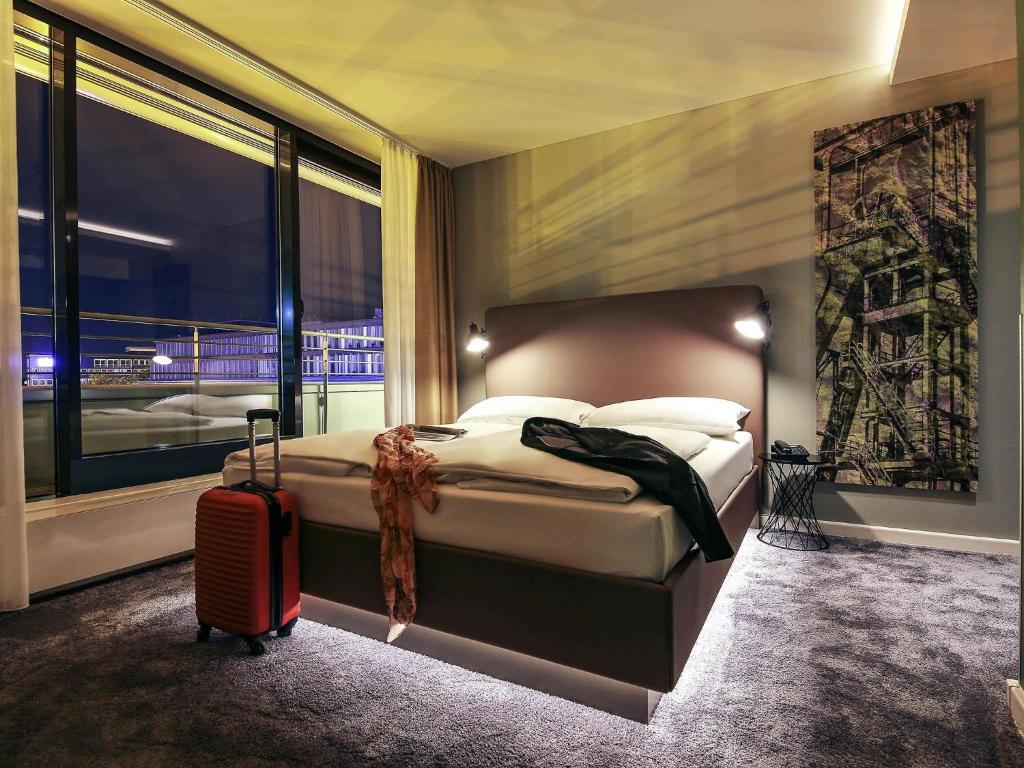 a bedroom with a bed with a suitcase and a window at Mercure Hotel Plaza Essen in Essen