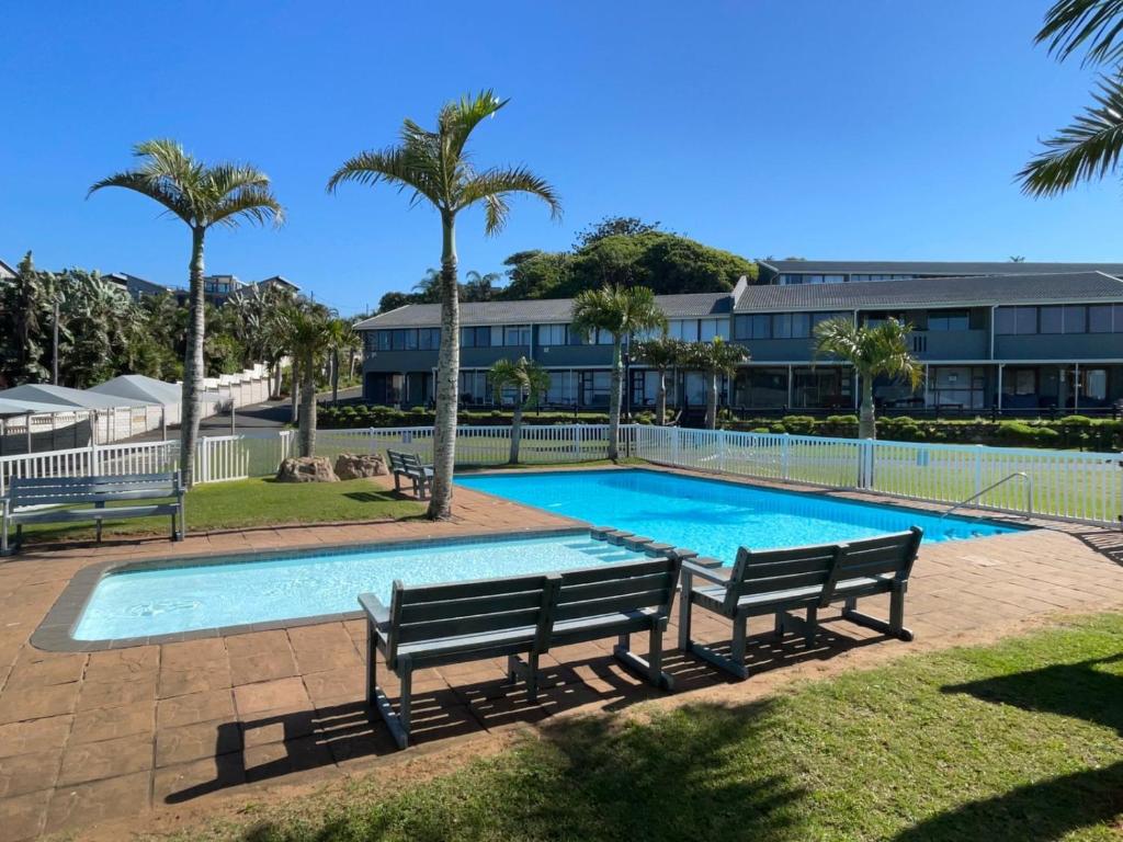 a swimming pool with two benches in front of a building at 3 Eden Sands in Kingsborough