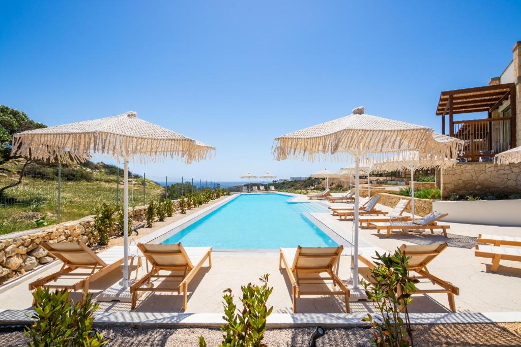 a pool at a resort with chairs and umbrellas at Ramnus Karpathos Suites in Karpathos
