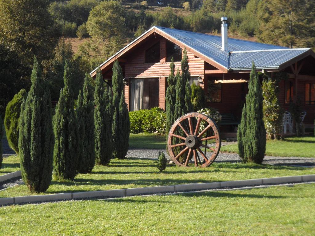 a cabin with a wagon wheel in front of a garden at Orillas del Coilaco in Pucón