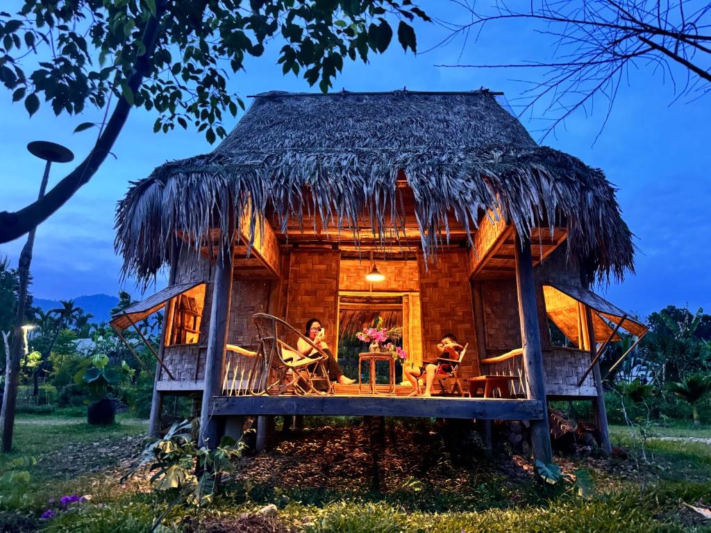a house with a thatched roof with people sitting in it at Dhami Farmstay, Đông Giang, Đà Nẵng in Danang